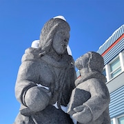 Une sculpture en granit devant un bâtiment, qui représente une femme et un enfant avec un livre à la main.