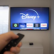 Une main tient une télécommande face à une télévision qui montre Disney+.