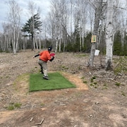 Un joueur de disque-golf s'apprête à lancer son disque au milieu des arbres.