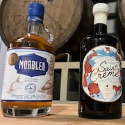 Deux bouteilles d’alcool sont déposées sur une table devant des barils en bois.