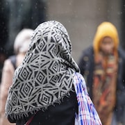 Une femme portant un voile marche sous une fine neige, à Montréal.