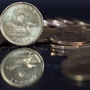 Une pièce d'un dollar, debout au milieu d'autres pièces de monnaie. 