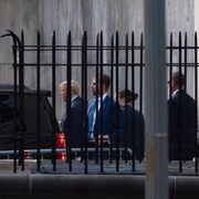 Donald Trump et d'autres personnes, qu'on aperçoit derrière une clôture.