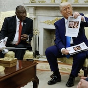 Donald Trump, assis à côté de Cyril Ramaphosa, montre la une d'un article.
