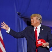 Donald Trump tient un casquette « save America » devant un drapeau américain.