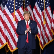 Donald Trump applaudit devant des drapeaux américains.