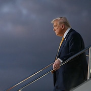 Le président américain Donald Trump descend d'Air Force One devant un ciel sombre.