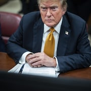 L'ancien président américain Donald Trump assis à une table avec en main des documents. 