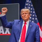 Le candidat républicain Donald Trump lève le poing. Derrière lui, deux drapeaux des États-Unis. 