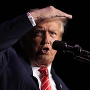 Donald Trump parle au micro en tenant sa main droite à la hauteur de ses cheveux.