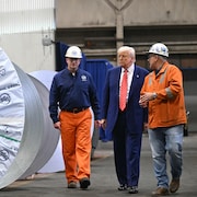 Donald Trump marche avec des travailleurs de l'acier à côté de gros rouleaux d'acier, le 30 mai 2025.