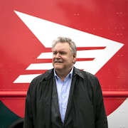 Doug Ettinger pose devant un logo de Postes Canada.