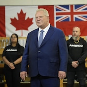 Il est devant des drapeaux de l'Ontario et du Canada.