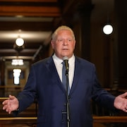 Doug Ford écarte les bras en parlant lors d'un point de presse.