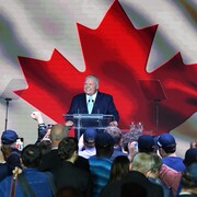 Il parle à ses partisans devant un immense drapeau canadien.
