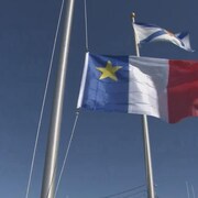 Le drapeau acadien en train d'être hissé au sommet d'un mât.