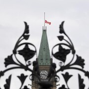 Le drapeau canadien en berne sur le Parlement, vu à travers la grille d'entrée.