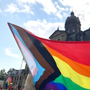Un drapeau de la Fierté tenu par un manifestant flotte au vent devant l'édifice de l'Assemblée législative du Nouveau-Brunswick.