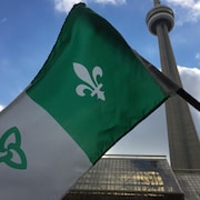 Un drapeau franco-ontarien tenu devant la Tour CN à Toronto.