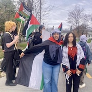 Deux élèves portant des keffieh regardent la caméra, tandis qu'on voit à l'arrière d'autres jeunes arborant des drapeaux palestiniens ainsi qu'une pancarte où il est écrit «1 solution, Intifada, Révolution!».