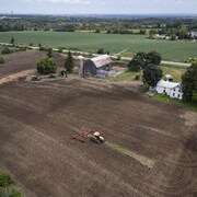 Vue aérienne d'une ferme et d'un tracteur dans un champ. Au fond, des espaces verts.