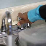 Une main de femme qui ouvre un robinet d'où coule de l'eau.