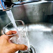 Une main remplit un verre d'eau dans un évier.