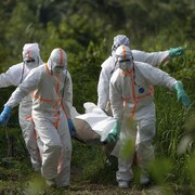 Des travailleurs funéraires en vêtements de protection portent les restes d’un homme mort d'Ebola. 