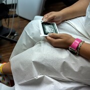 Une femme assise, dont on ne voit que les jambes et les mains, tient l'image imprimée d'une échographie.