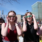 Trois personnes regardent l'éclipse partielle du 8 avril 2024 à Calgary, à travers des lunettes de protection. 