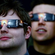 Deux hommes portant des lunettes pour éclipse regardent le ciel.