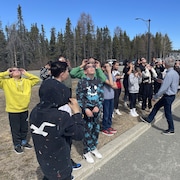 Des élèves et des enseignants sont rassemblés à l'extérieur et regardent vers le ciel avec des lunettes protectrices.