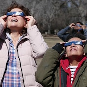 Deux femmes observent l'éclipse solaire partielle au Centre des sciences de la Saskatchewan, à Regina, le 8 avril 2024.