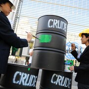 Des manifestants peignent un baril de pétrole avec de la peinture verte.