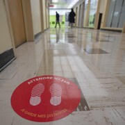 Un couloir d'une école avec, sur le sol, des consignes de distanciation.