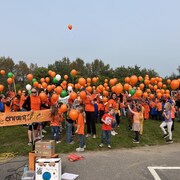 Des jeunes qui portent des chandails orange tiennent des ballons dans leurs mains.