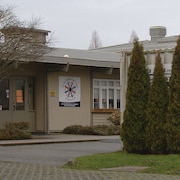 L'entrée de l'école vue de l'extérieur, avec le logo de l'école, et une partie d'un bâtiment un peu désuet avec quelques arbres devant.