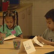 Deux enfants assis à une table écrivent leur nom sur des cartons.