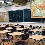 Une salle de classe vide avec un tableau, des tables et des chaises.