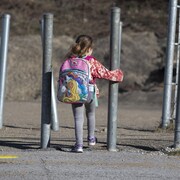 Une petite fille, de dos, portant un sac d'école.