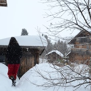 Dans un paysage hivernal, une femme marche, à travers des maisons de style alpin