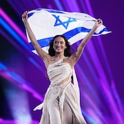 Une femme marche sur une scène en souriant et brandit un drapeau israélien.