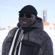 Un homme d'origine africaine avec son manteau d'hiver et son foulard tout sourire à l'extérieur.