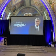 Dans le chœur de l'église, un grand écran montre une photo de Brian Mulroney. 