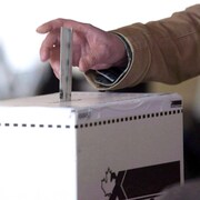 Une main tient un bulletin de vote et la dépose dans une urne électorale. 