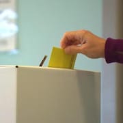 Une main dépose un bulletin de vote dans une boîte.