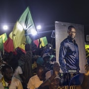 Plusieurs personnes sont rassemblées et tiennent des drapeaux du Sénégal et des photos des candidats à la présidentielle. 