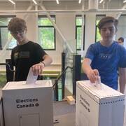 Deux jeunes élèves mettent des bulletins de vote dans les urnes.