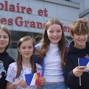 Quatre élèves tiennent des drapeaux francophones de Terre-Neuve-et-Labrador devant leur école.