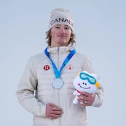Il pose avec sa médaille et une petite peluche de la mascotte des Jeux de olympique de la jeunesse. 